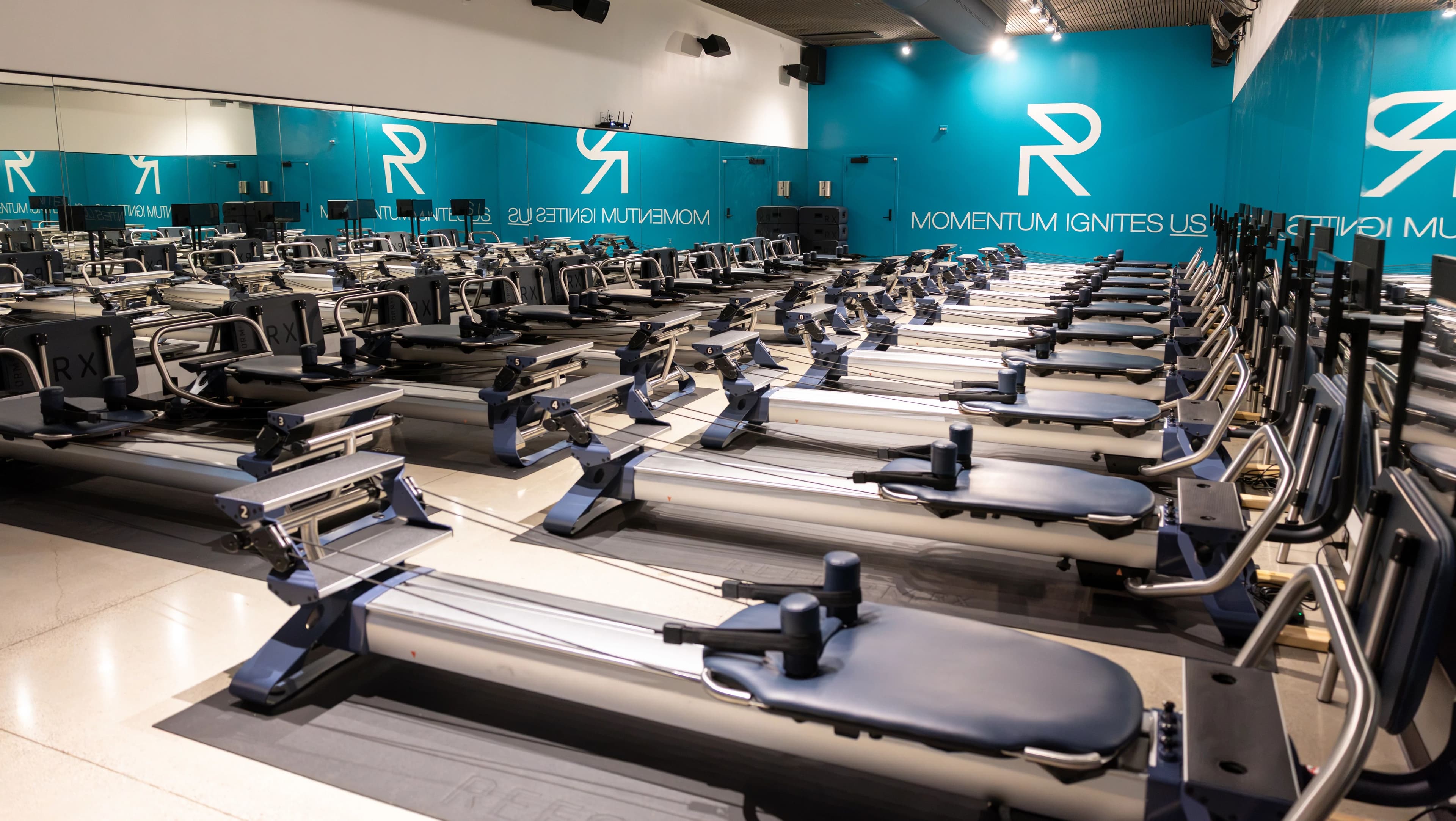 A fully equipped commercial Pilates reformer studio with 20-plus machines in rows, showing the multi-machine floor format sports performance facilities and fitness clubs are adopting for athlete recovery and group training.