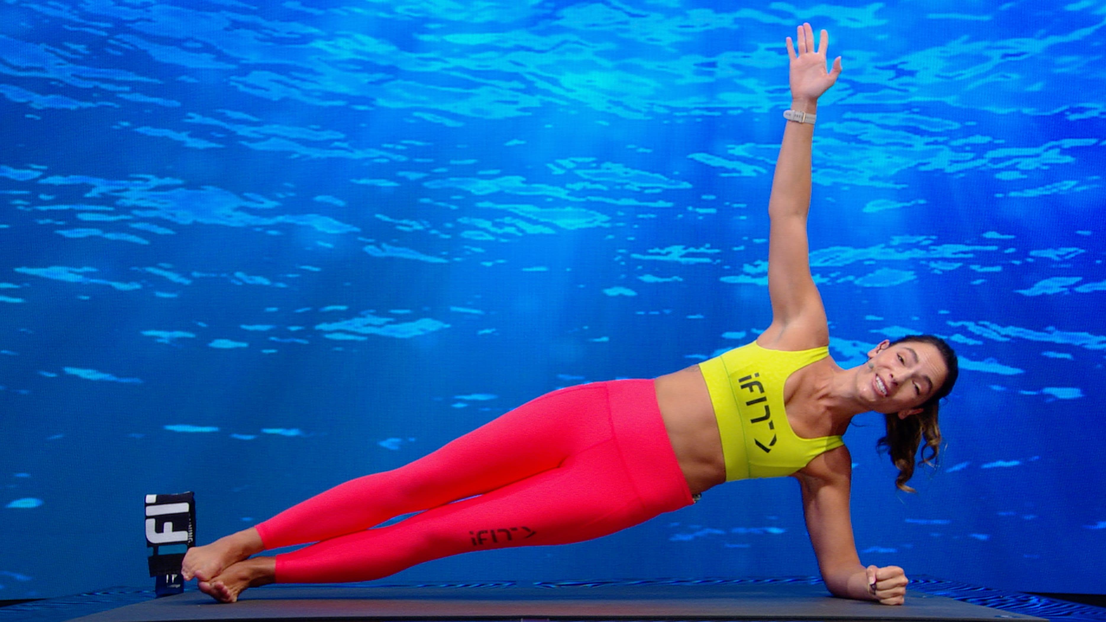 Woman in a side plank position on a mat, one arm raised overhead, demonstrating a Pilates core stability exercise