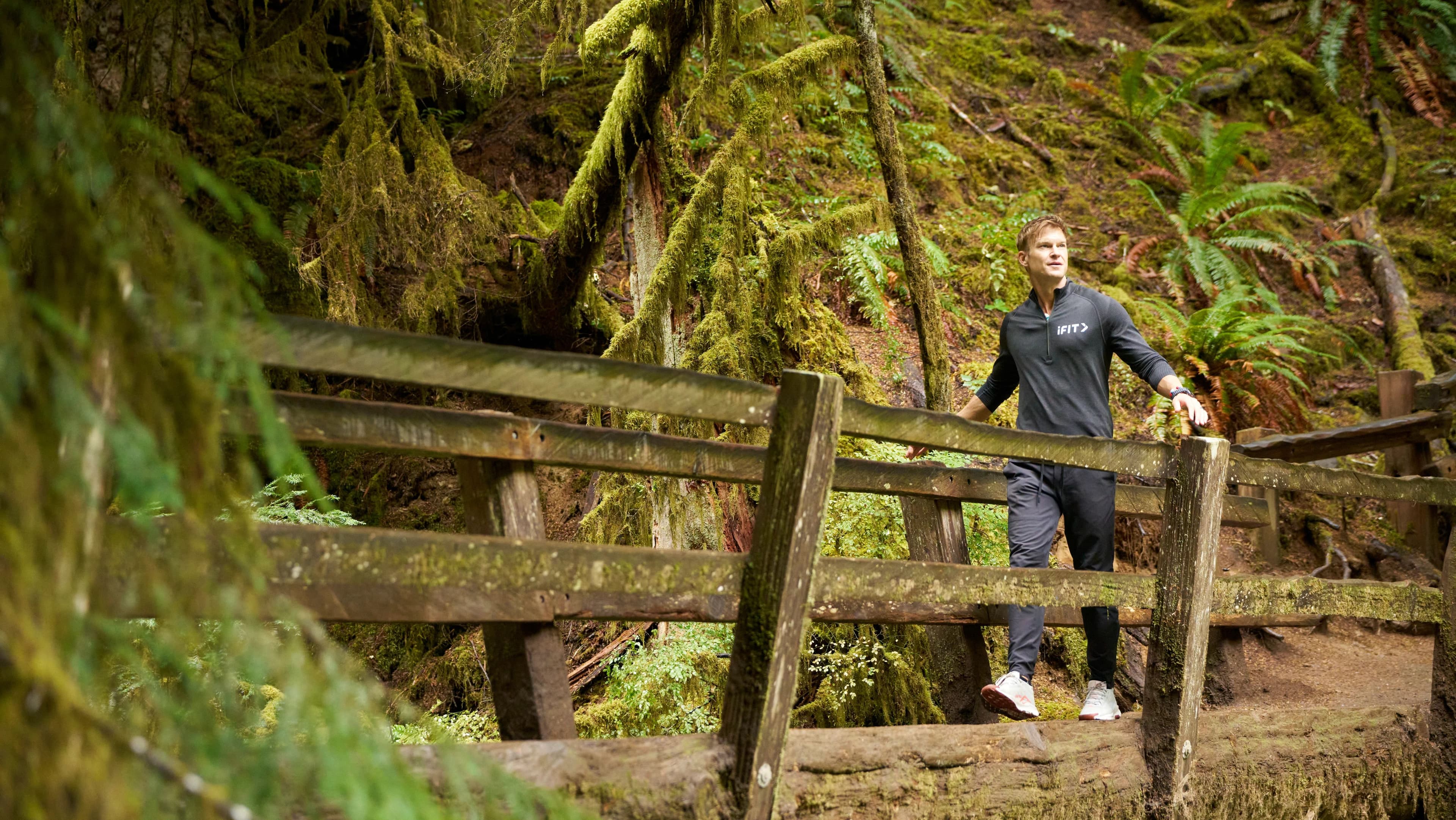 iFIT Trainer John Peel pauses on a mossy wooden boardwalk trail during the Olympic National Park Walk + Hike Series workout.