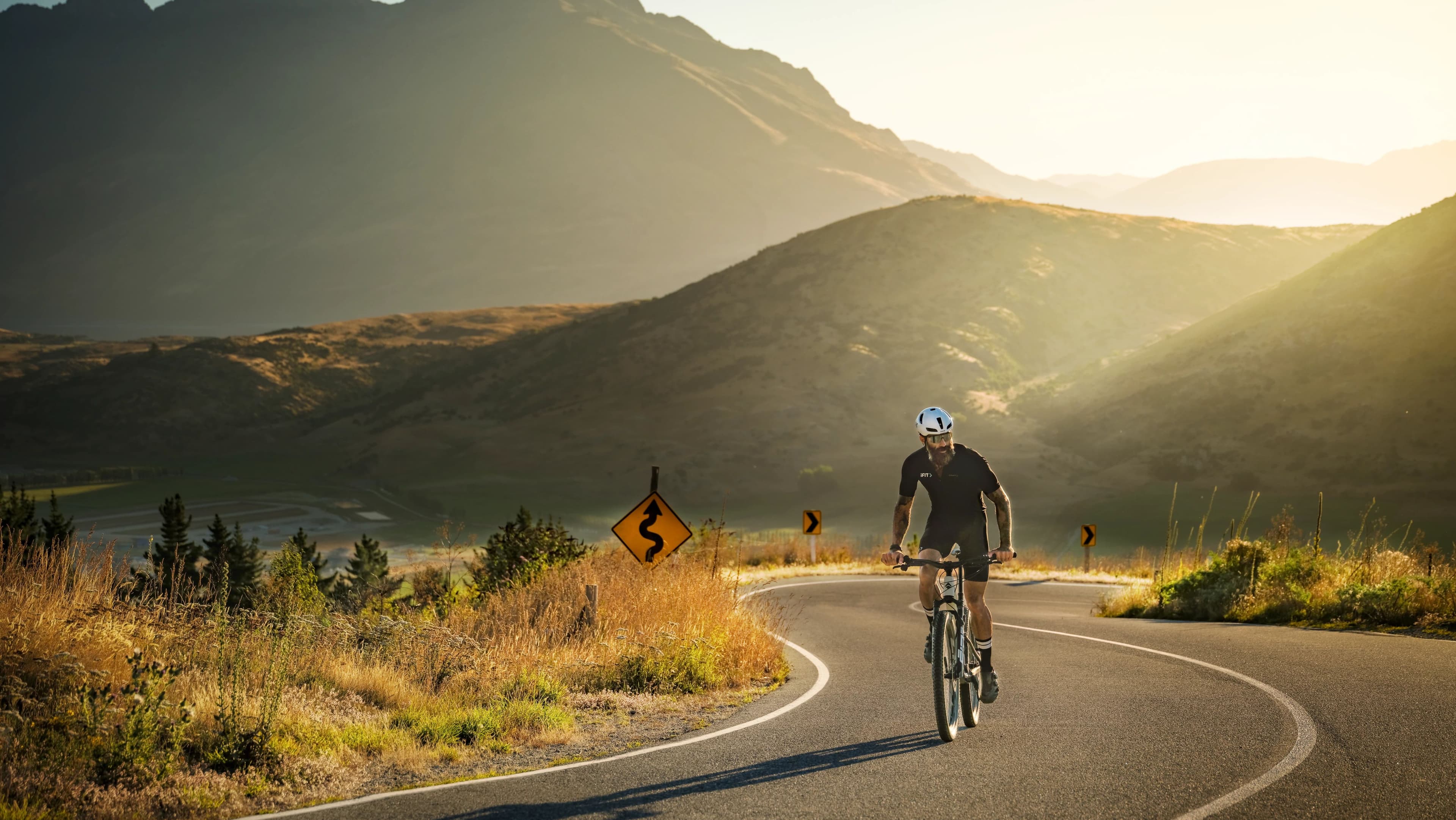 A cyclist in iFIT gear riding a winding mountain road in New Zealand during the Biking Basics: New Zealand series with trainer Tommy Rivs