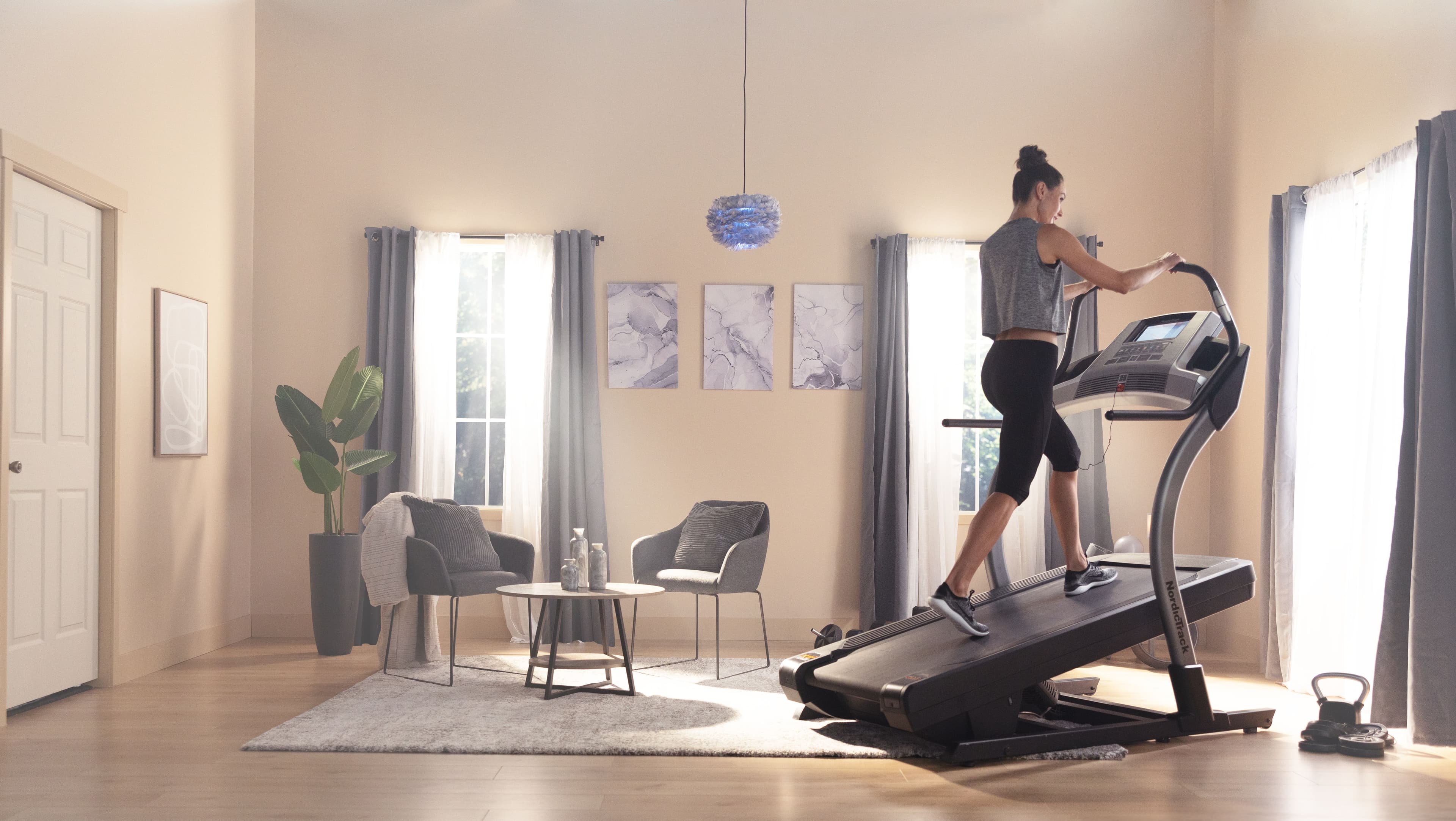 Woman running on an inclined NordicTrack treadmill in a home living room, demonstrating terrain-driven incline training