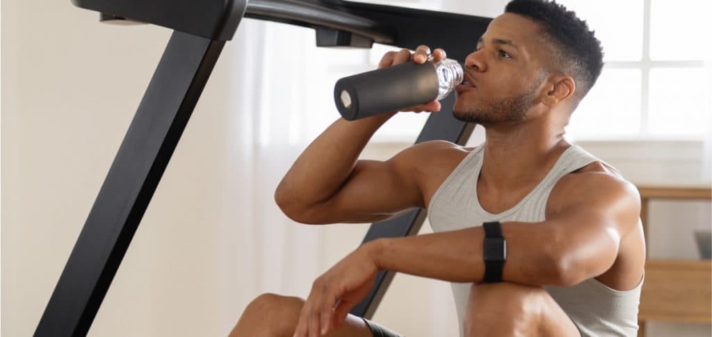 Individual drinking water beside a treadmill during a home workout, highlighting the importance of hydration while using GLP-1 medications.