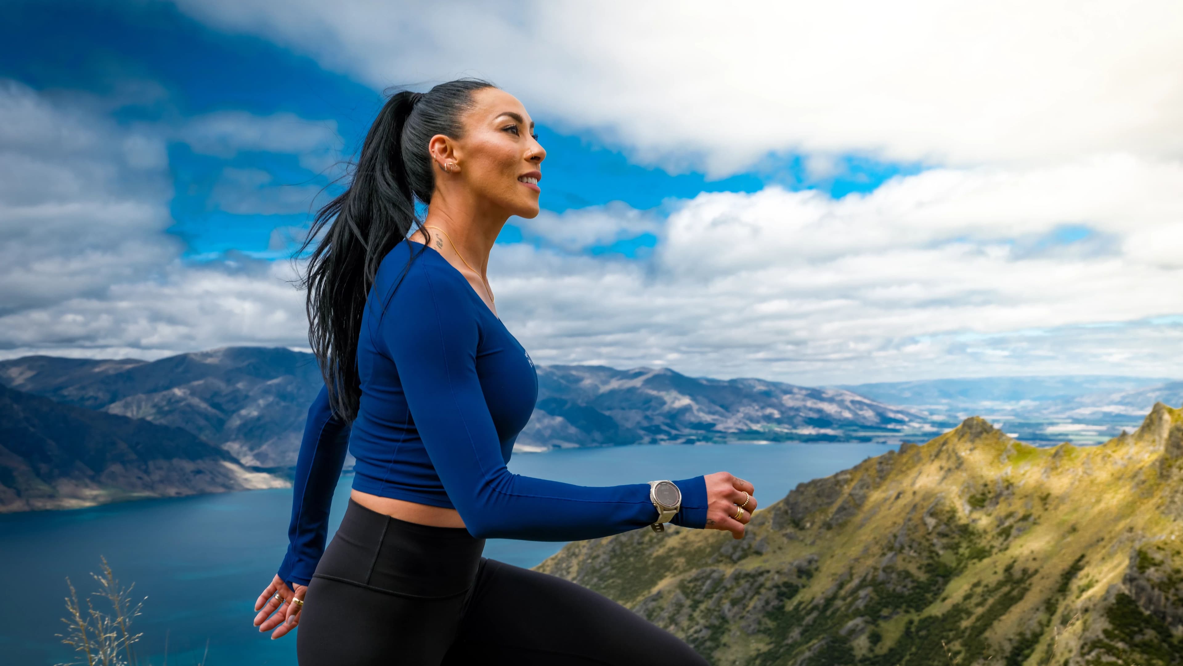 iFIT trainer Hannah Eden hiking at elevation in New Zealand with mountain and lake views behind her, from the iFIT New Zealand 12-3-30 Hiking Series