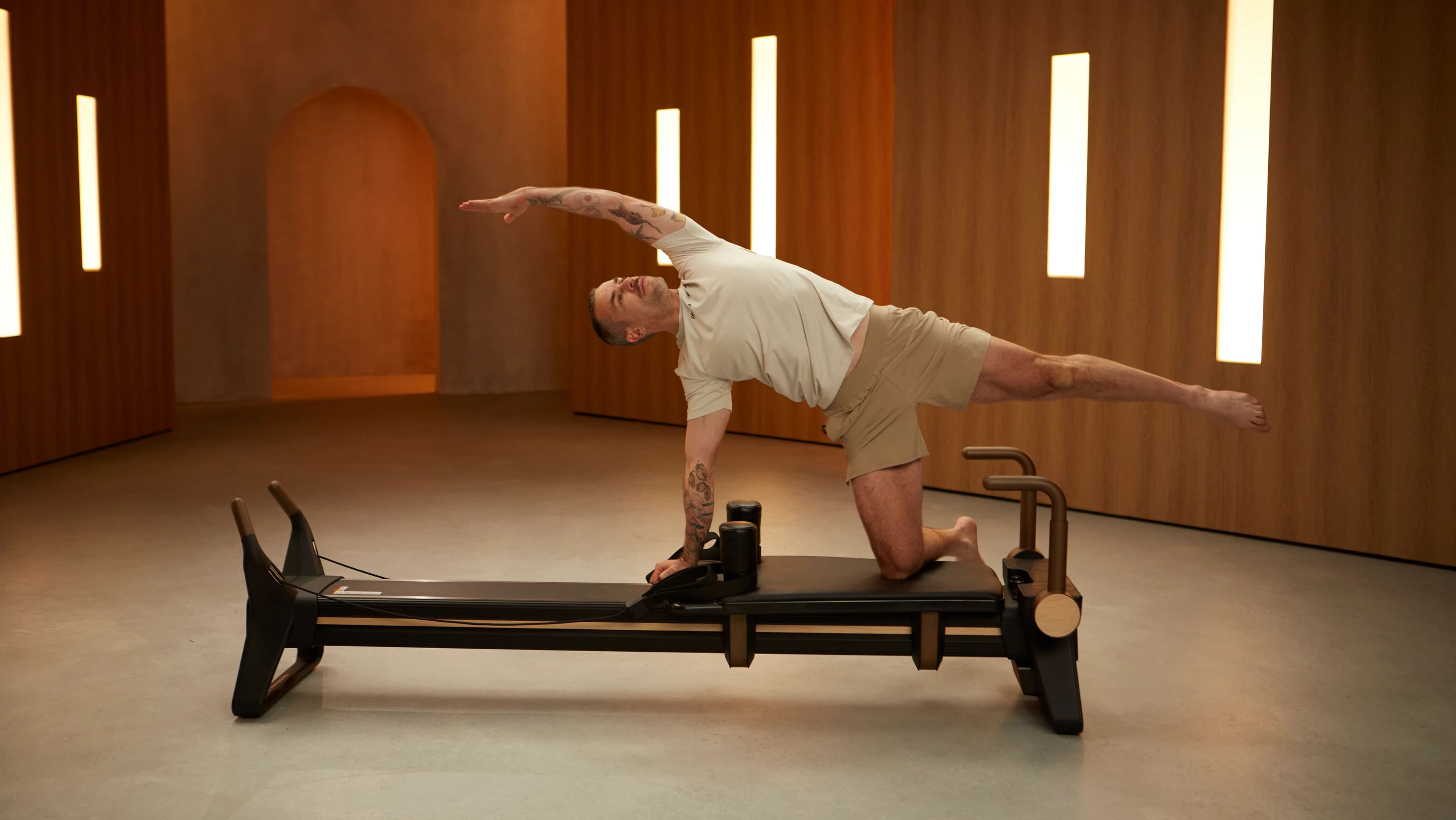 iFIT trainer Abe Ahern demonstrates a lateral reach on the NordicTrack Ultra 1 Reformer in the Base to Burn Pilates series — available with the Reformer Digital Activation.