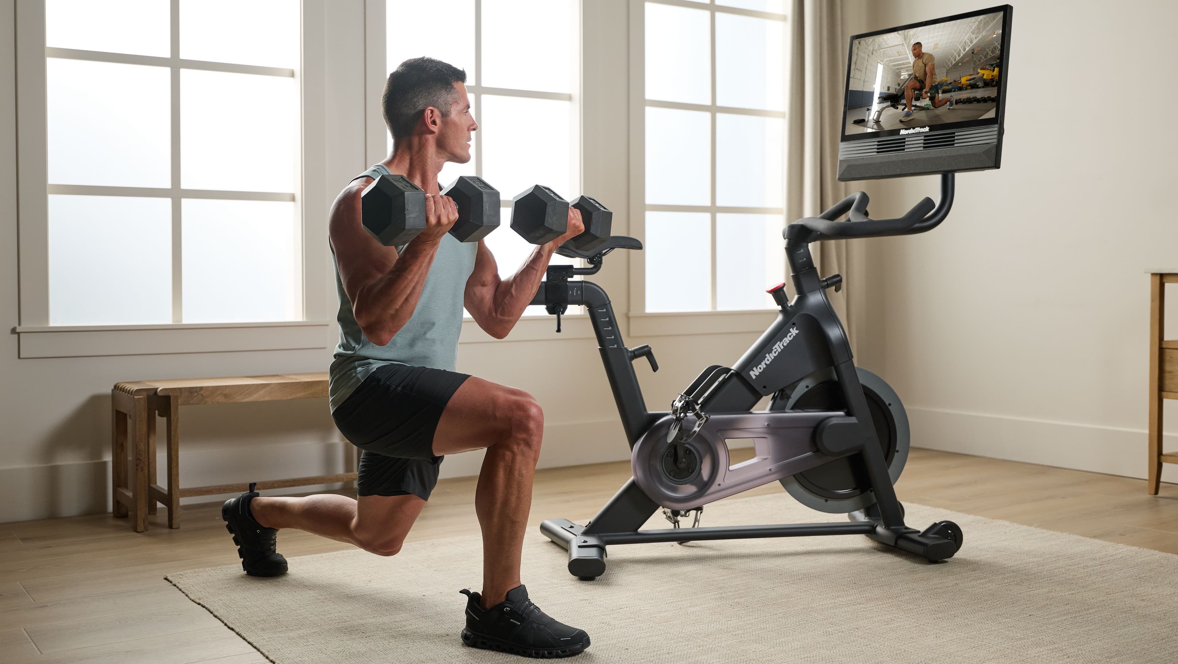 Man performing a dumbbell lunge beside the NordicTrack X24 Bike, following an off-bike strength segment on the touchscreen