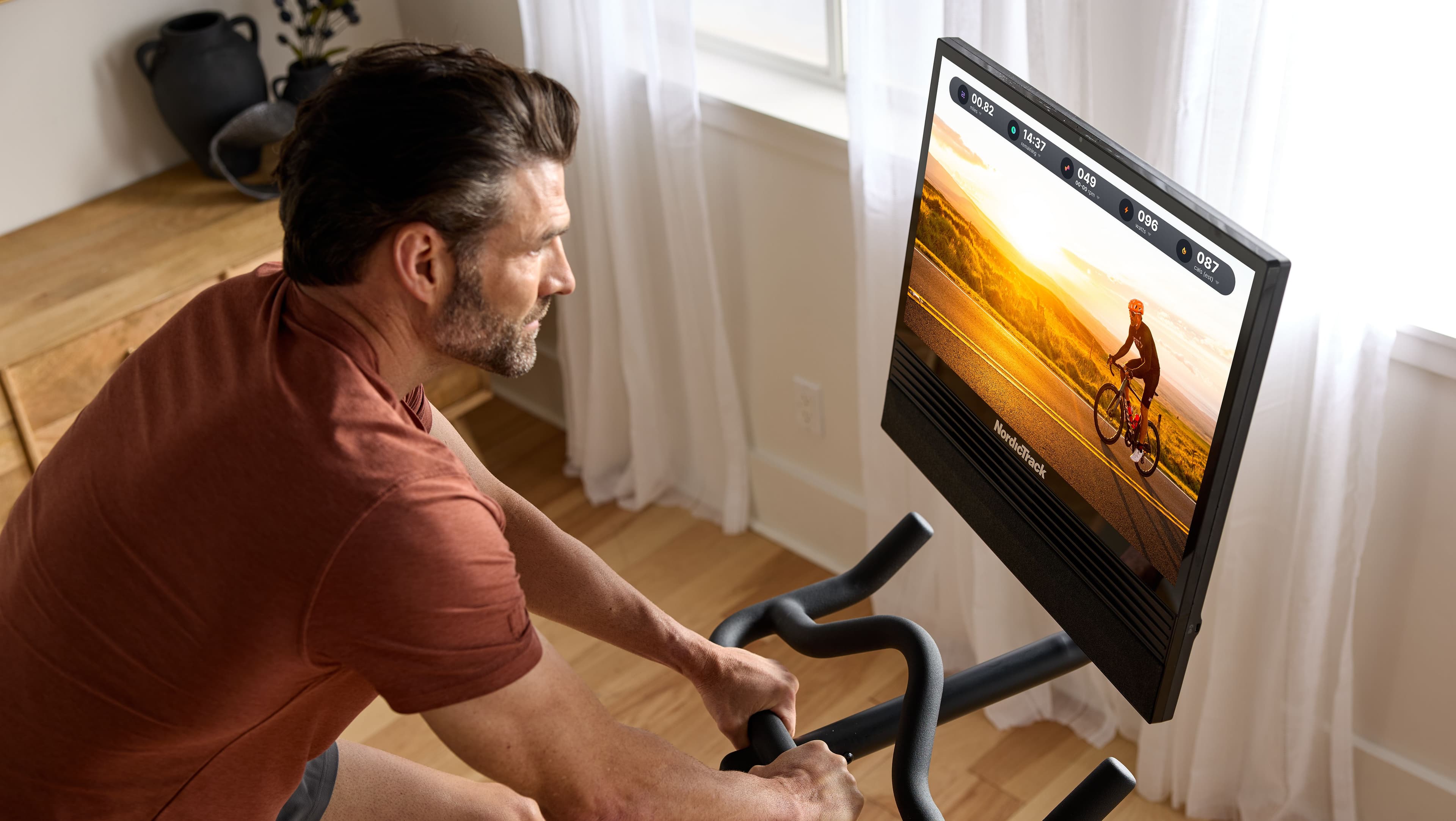 NordicTrack S24 Studio Bike with iFIT guided workout on 24-inch HD touchscreen, showing real-time metrics and an outdoor cycling route for home cardio training