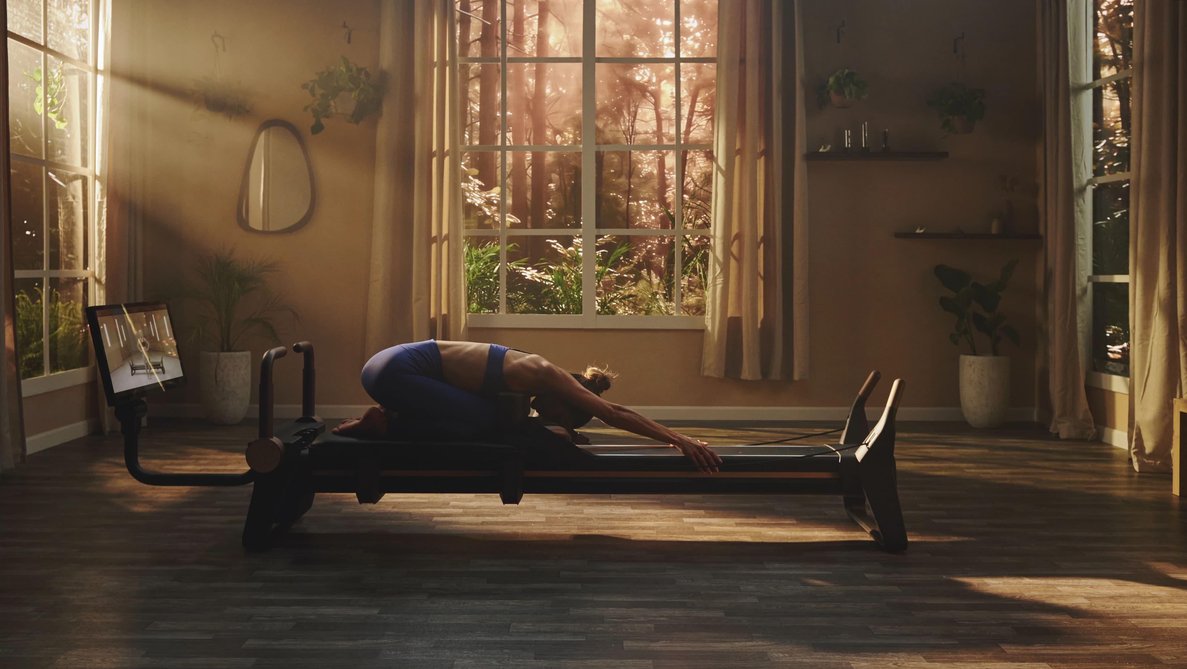 A practitioner performs a deep spinal stretch on the NordicTrack Ultra 1 Reformer in a sun-drenched, botanically styled wellness room with iFIT on screen. The atmosphere luxury spas are creating around connected reformer programming.