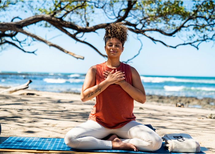iFIT  Trainer Meditating on a Beach and Practicing Stress-Reducing Techniques While Holding Her Heart Center