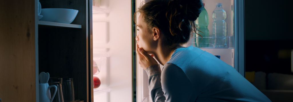 Curbing-After-Dinner-Cravings Alt text: Woman Looking Into a Fridge Late At Night for the Article How to Curb After Dinner Cravings